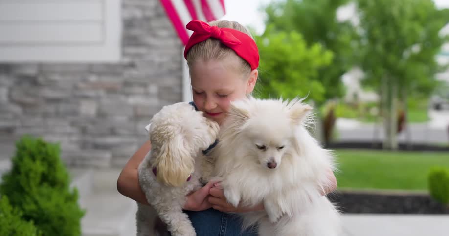 Little girl holding two dogs and giving them a kiss