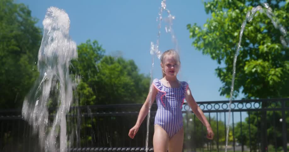 Young girl in a swimsuit runs through water coming up from a spout at a splash pad