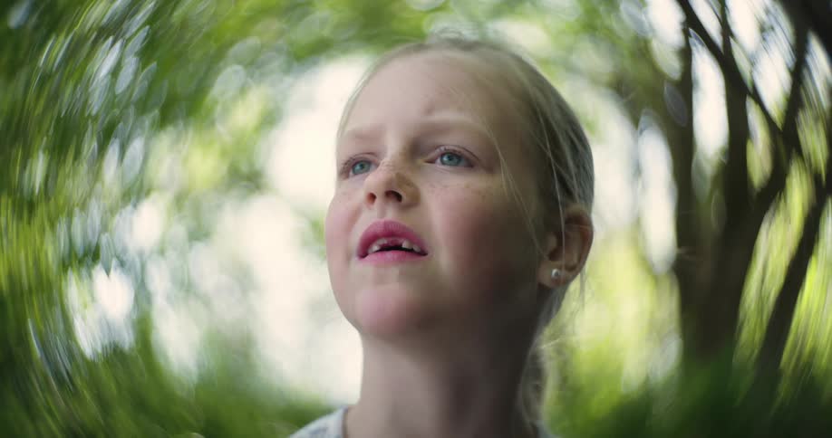Portrait of a little blonde girl with blue eyes, missing teeth, and freckles with trees in the background