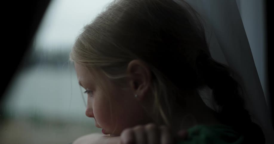 Girl leans her head on her arm while she stares out the window while it rains outside