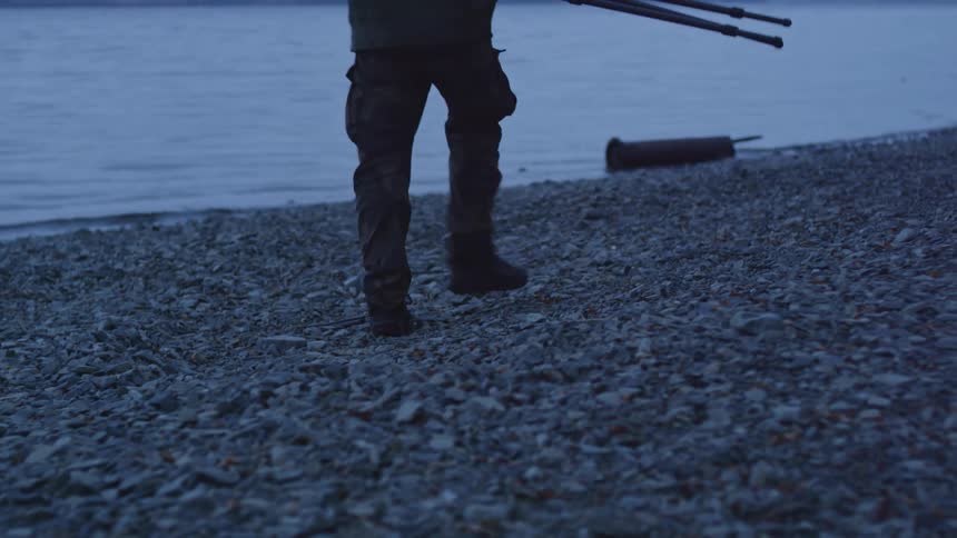A man sets up a camera and tripod on a rocky beach in front of the ocean
