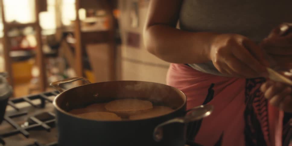 A person placing slices of food to cook in a pan on the stove as steam rises