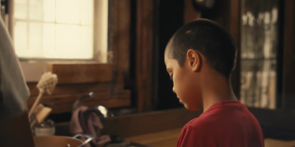 Young boy with a buzz cut concentrating on a task in a warm rustic room