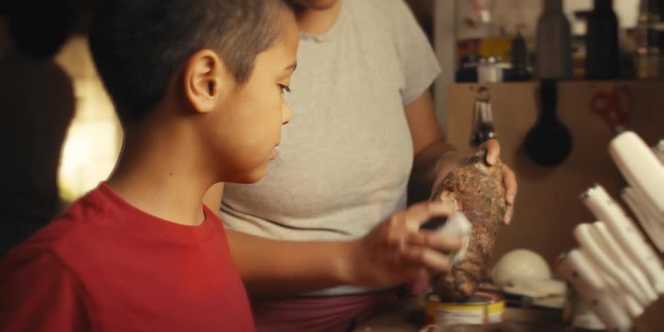 Boy watching his mother peel a vegetable