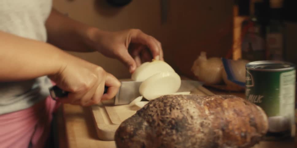 A young woman chops an onion on a wooden cutting board