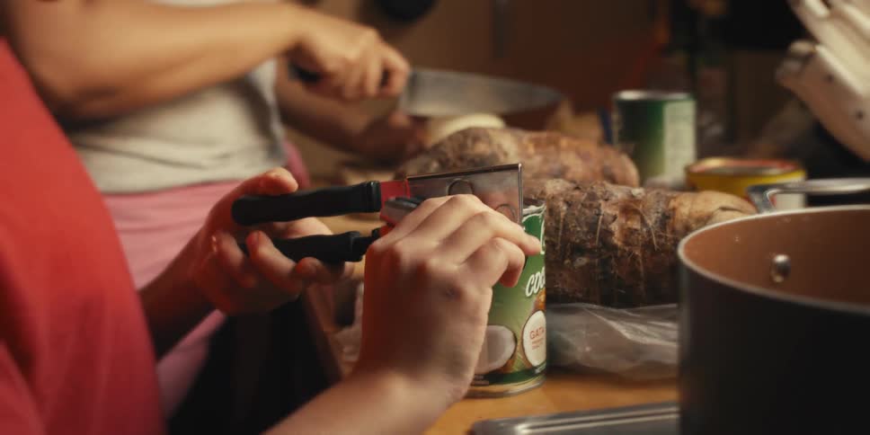Boy opening a canned food next to his mother in the kitchen