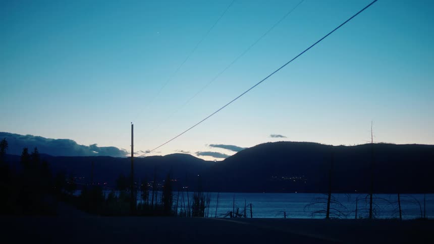 Convertible car passing by a lake with the silhouette of mountains on the horizon