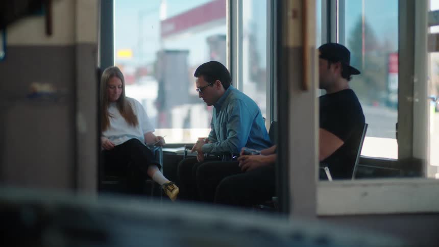 Three people are sitting in a waiting room and one man is looking restlessly to the side