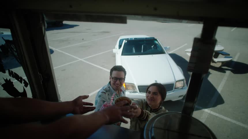 A couple smile as they accept their food from a food truck in a parking lot