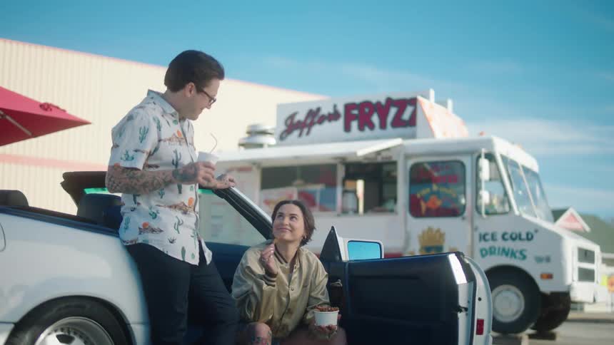 Couple in a convertible car next to a producer drinking and eating