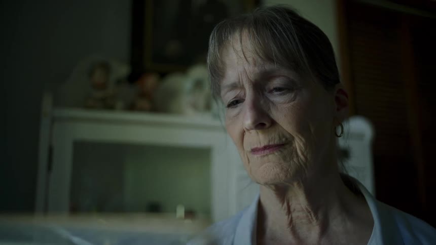 An elderly woman smiles while holding a photograph and looking at it
