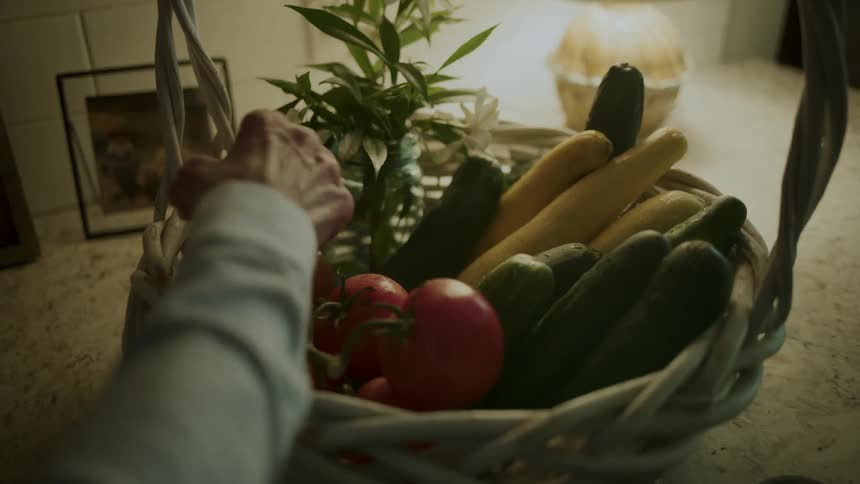 Person adds tomatoes to other produce in a basket on the counter