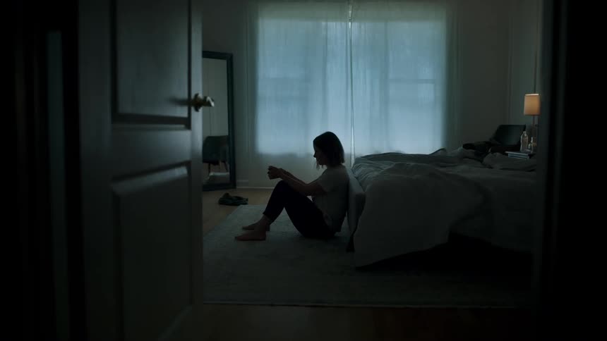A person sitting on a carpet in a room and leaning against a bed