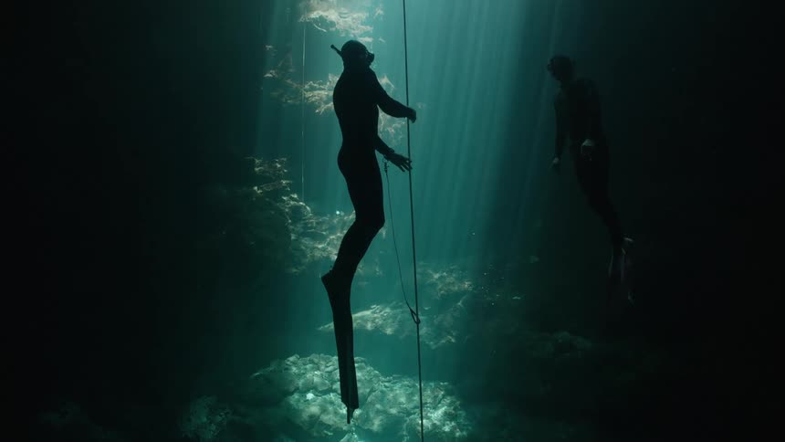 Silhouette of two divers at the bottom of an ocean climbing up through a rope