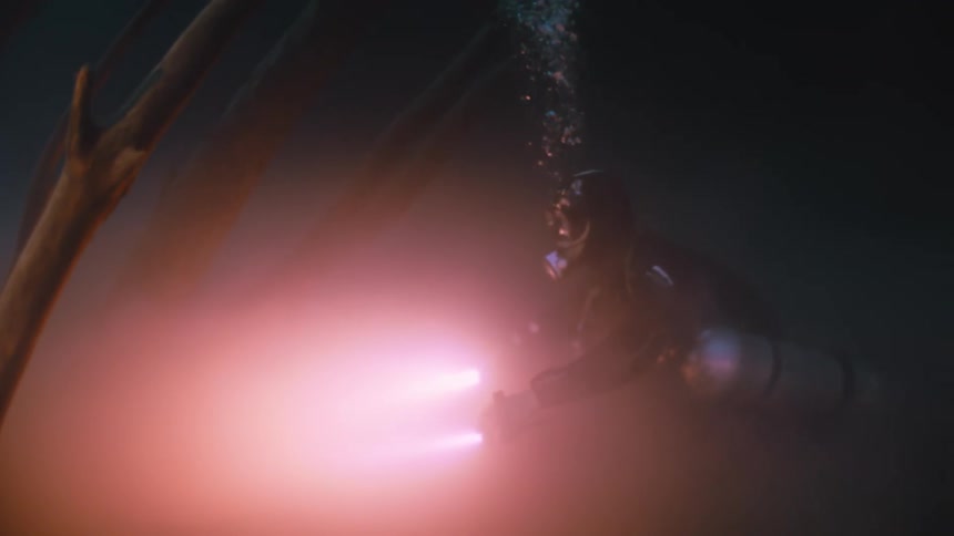 Diver using red lights on the bottom of an ocean with tree trunks