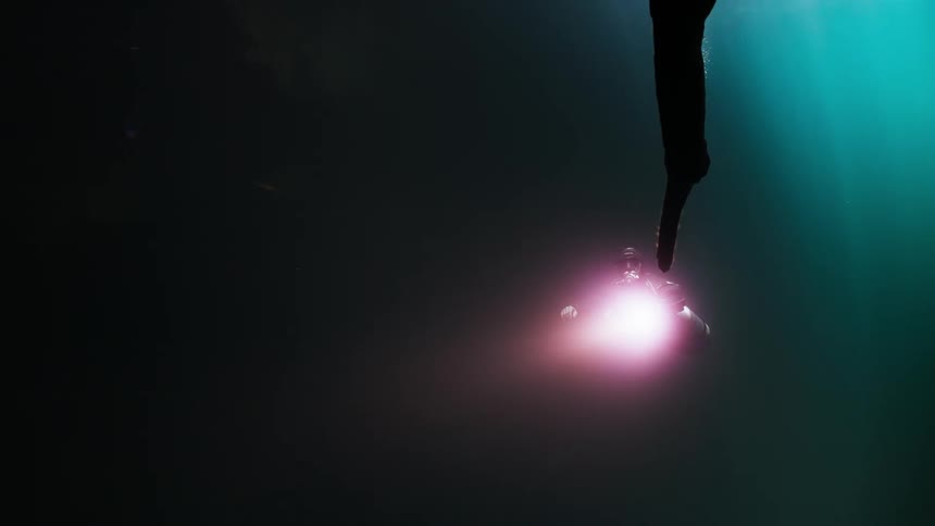 Diver venturing out with a flashlight and a vast dark ocean