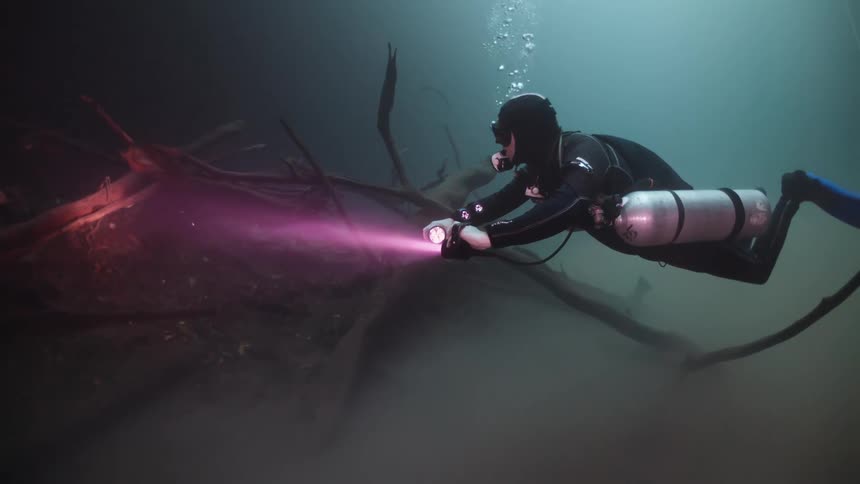 Person submerged in an ocean using an oxygen cylinder and a red light