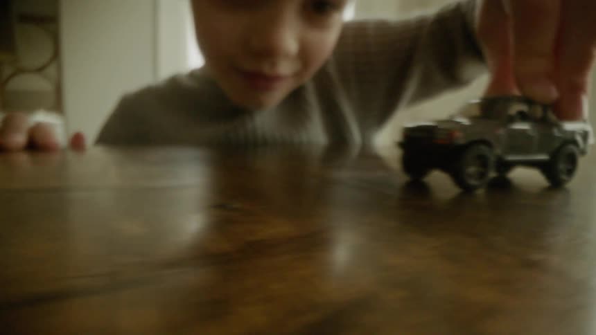 A young child plays with a small grey toy truck