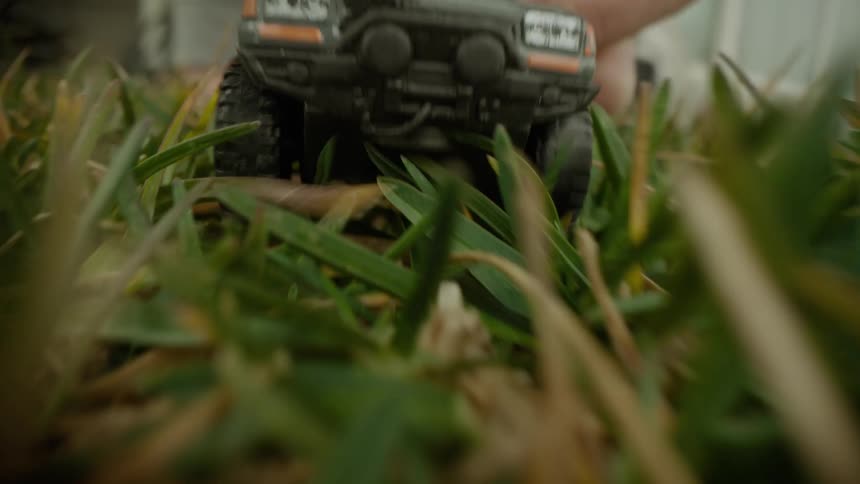Hand holding a toy car and moving through the grass