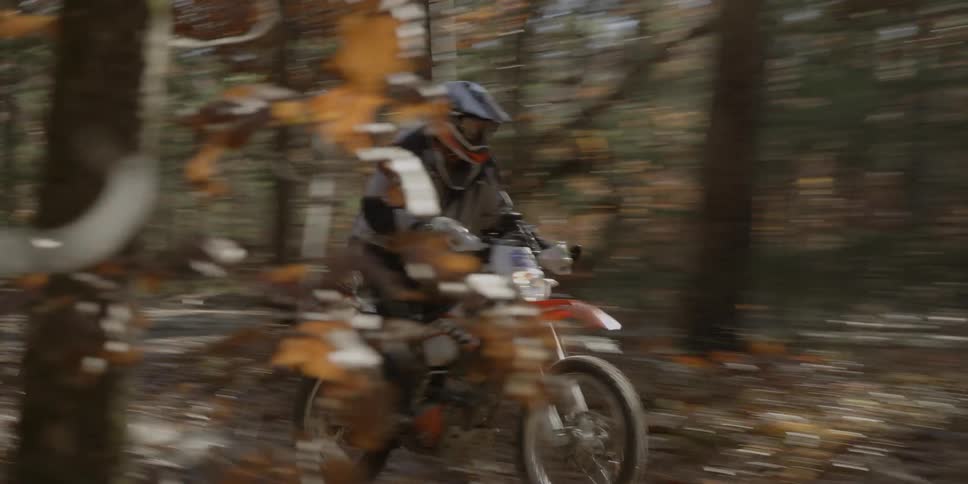 A man rides a motorcycle through a forest