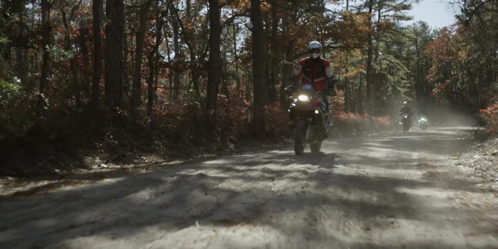 People riding dirt bikes on a dirt road surrounded by trees
