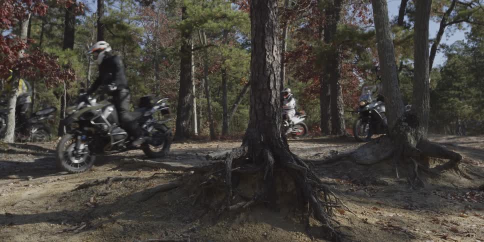 Dirt bike riders ride through a forest trail