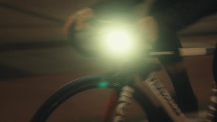 Close up of a persons hands holding the handlebars of a bicycle with a flashlight moving through the streets at night