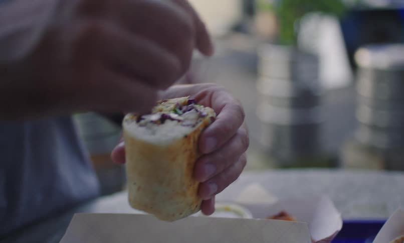 A person holding a food and is putting a sauce on top