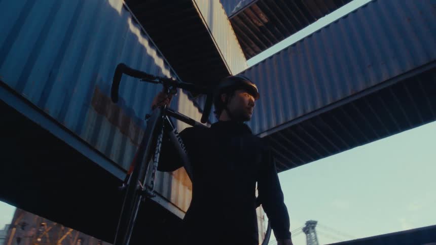A cyclist carrying a bicycle under a tower made of alternating cargo containers
