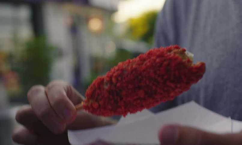 A close up of a persons hand holding a red battered deep fried food item