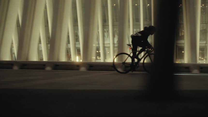 Person on a bicycle pedaling in front of a large set of windows lit from within