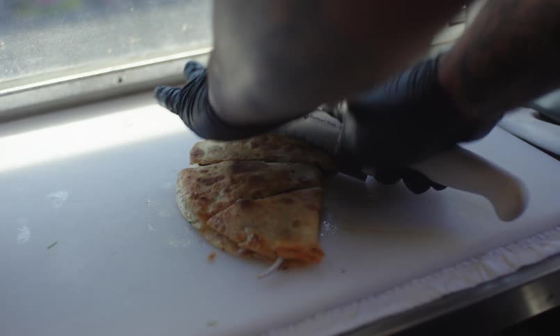 A mans hand is cutting slices into a quesadilla