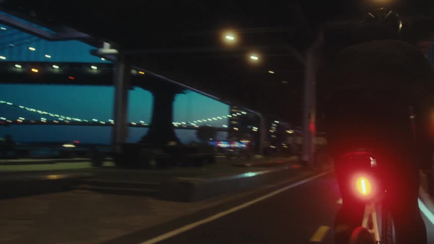 A man riding a bicycle on a city road under a bridge by a river passing cars and other cyclists