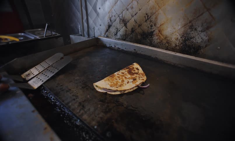 A quesadilla is cooking on a grill inside of a food cart