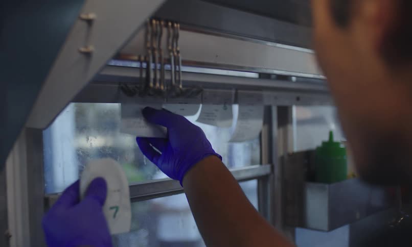 Person wearing a blue glove reaches into a shelf in a commercial kitchen with food order slips