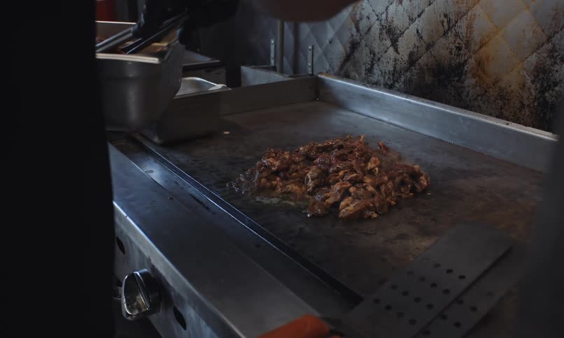 Chef cooking a pile of shredded meat on a flattop grill