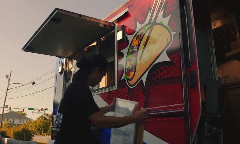 Red food truck with an illustration of a taco and a person closing a sign in front