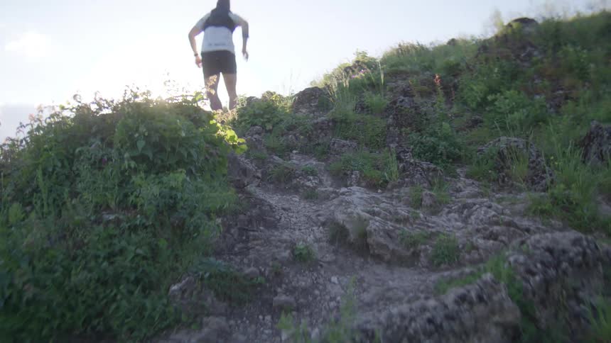 A white man runs up a rocky path on a hill