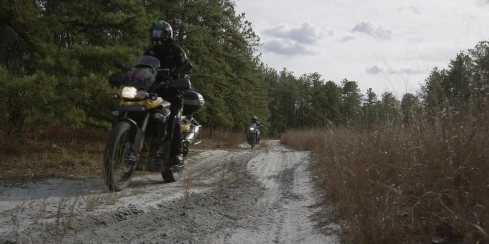 Motorcyclists are riding on a dirt road in a forested area