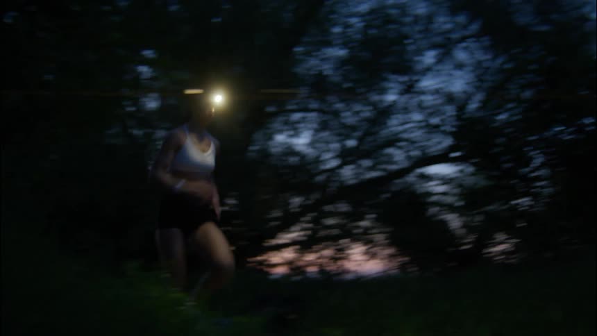 A woman jogging across a forest with a lantern on her head