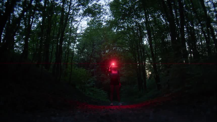 Man standing in a forest at dusk turning off the red light of a flashlight on his head