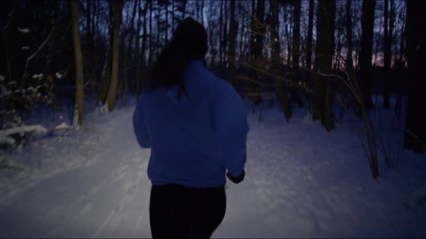 A woman runs through the woods as the sun sets