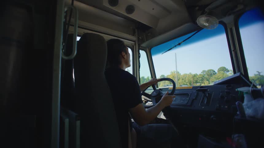 An asian mans drives a large truck through a suburb