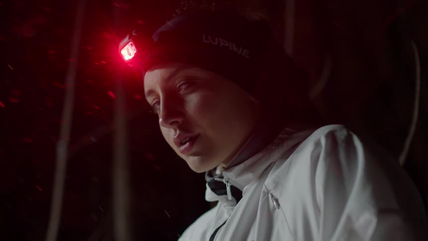 Woman wearing a headlamp smiles as the snow falls around her