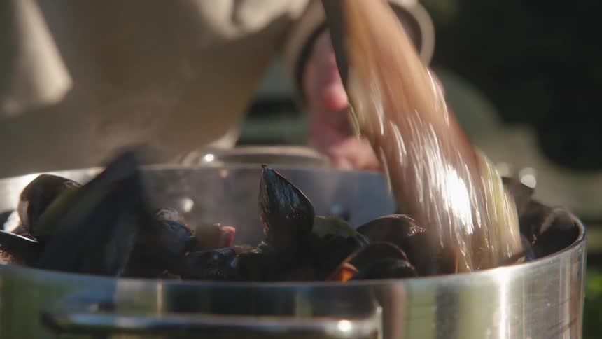 A close up of a cooking pot with mussels and vegetables being stirred