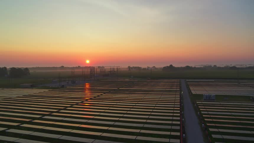 Solar panels in a rural area reflect light from a sinking sun