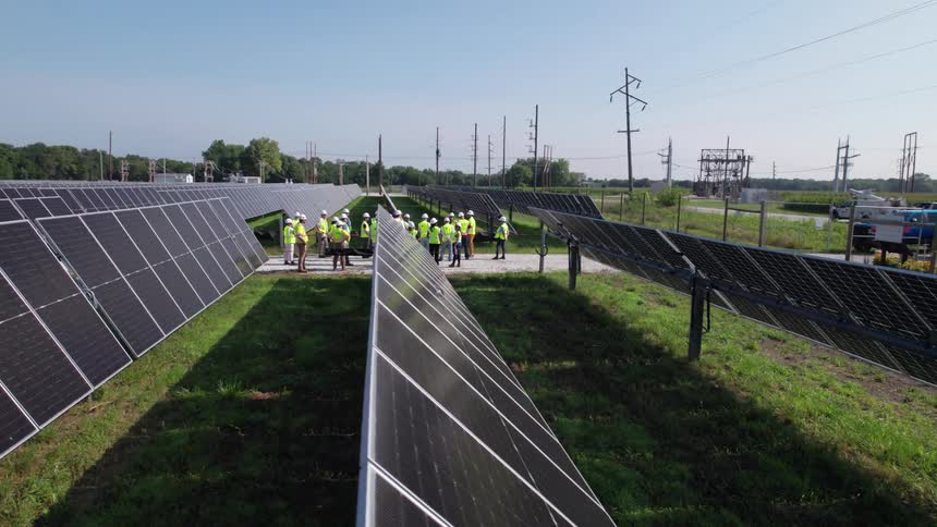 Field of solar panels with several individuals wearing safety vests in the background