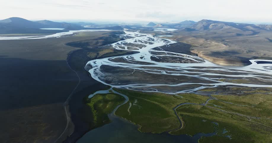 Multiple streams lead from a lake and across the fields between mountains on a cloudy day