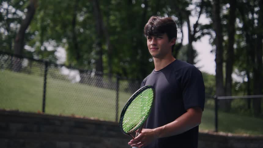 Teenage boy twirls a tennis racket before setting his stance on the court