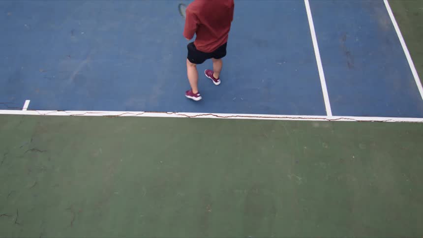 A man in a red shirt is serving a tennis ball on a blue and green court